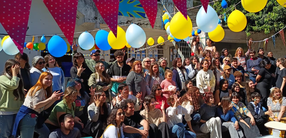 Un grupo de personas se toman una fotografía grupal en un patio que está decorado con globos y banderines